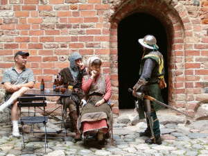 Kuva H&auml;meen Linnan sis&auml;pihalta keskiaikamarkkinoilta 2004. Kuvassa haarniskaan pukeutunut mies seisoo ja juttelee istuvan naisen ja kahden miehen kanssa. Yksi mihist&auml; on nykyaikaisessa puvussa kun muut ovat keskiaikaisissa puvuissa. Tuolit ja p&ouml;yt&auml; ovat my&ouml;s nykyaikaisia. (c) Anne Mets&auml;puro